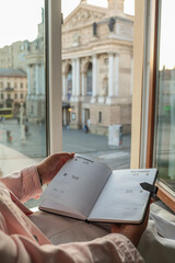 Woman holding a planner open to early September while sitting by a window with a view of the Lviv...