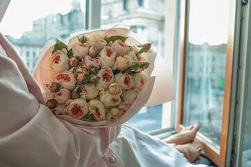 Woman holding a bouquet of delicate pastel roses by an open window with a view of Lviv Opera House....