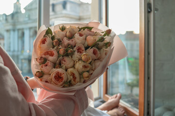 Woman holding a bouquet of delicate pastel roses by an open window with a view of Lviv Opera House....
