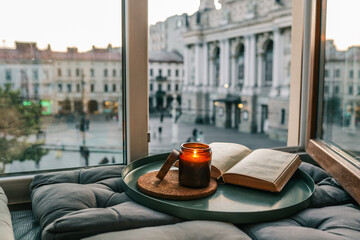Open book and lit candle on a cozy windowsill nook with cushions, overlooking the Lviv Opera House....