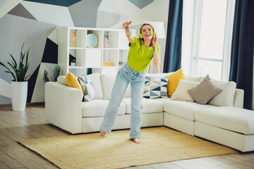 Young woman enjoying music and dancing at home, wearing green t-shirt and jeans, in a modern living...