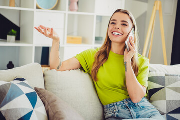 Happy young woman talking on smartphone while relaxing on cozy couch in modern living room with...