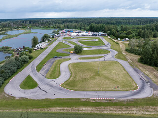 A go kart track with marked lanes and barriers, surrounded by grassy fields, a forested region, and...