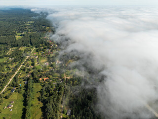 Aerial perspective of a rural area with low lying clouds, scattered houses, open fields, forest...