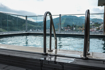 Modern rooftop pool with stainless steel ladder and glass fence. Water reflects cityscape and...