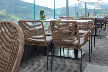 Outdoor terrace with wicker chairs, tables, and glass fence overlooking mountain landscape. Cozy...