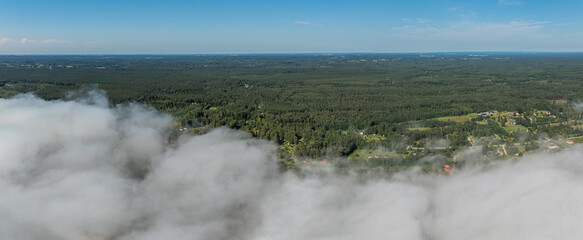 Forested land extends to the horizon under a clear sky, with low clouds and scattered buildings visible, highlighting a remote rural area.