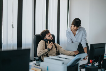 Two colleagues are working collaboratively in an office environment, discussing and reviewing a...