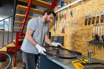 Skilled bike mechanic man using tools repairing bicycle in well-organized workshop