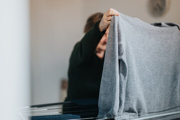 An elderly woman dries clothes on an indoor rack, symbolizing daily routines and household chores...