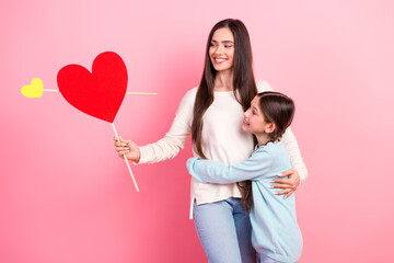 Smiling mother bonding with young daughter holding heart display against pink background...