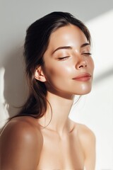 Beauty portrait of young woman with glowing skin and closed eyes on white background.