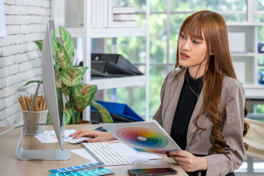 Asian female graphic designer analyzing color palette at modern workspace