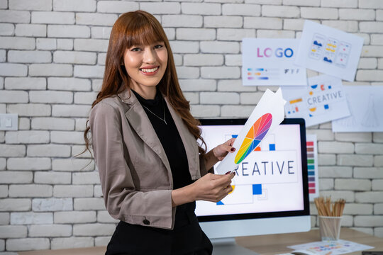 Asian female graphic designer holding color palette in creative design office, looking at camera