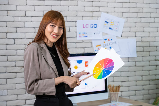 Asian female graphic designer presenting color wheel in modern creative office, looking at camera