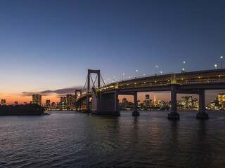 Tokyo's Rainbow Bridge at twilight, offering a stunning view of the city skyline and Odaiba. The...