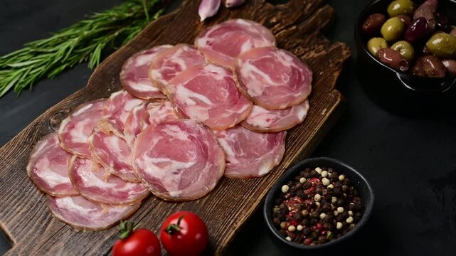Sliced coppa capocollo arrangement with herbs, peppers, and olives on rustic wood