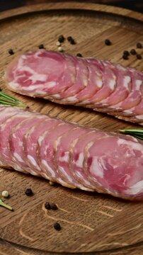 Delicious charcuterie presentation of sliced capocollo with rosemary and peppercorns on wooden board