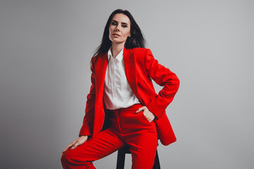 Confident businesswoman posing in red formal suit on gray background with elegance and...