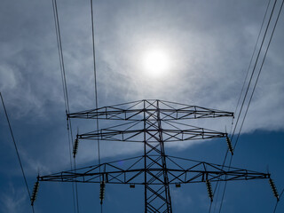 Silhouette of a high-voltage power transmission tower set against the bright sun and dramatic sky....