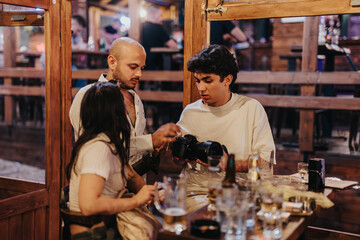 A group of friends enjoys their time together in a cozy wooden cafe, discussing camera details and...