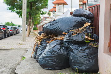 Large black plastic bags filled with garden waste and dry leaves placed on the sidewalk in a residential neighborhood, awaiting garbage collection.