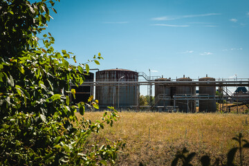 Greenery embraces industrial tanks under a clear blue sky in a rural setting showcasing nature and...