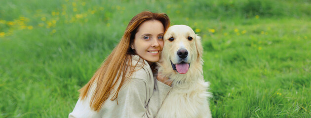 Happy owner young woman with Golden Retriever dog sitting on grass together in summer park