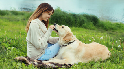 Happy owner young woman feeding Golden Retriever dog on the grass together in summer park