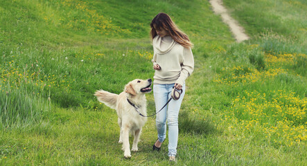 Owner woman walking with Golden Retriever dog on leash in summer park