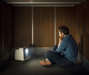 Lonely sad man watching the atomic bomb explosion on TV in a small room