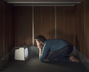 Scared man in a small room watching a television with no signal