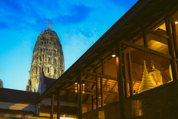 Fototapeta premium Cultural heritage Wat Mahathat Worawihan, Ratchaburi, Thailand. Low angle shot of Buddha head in golden dusk light, ancient Dvaravati chedi and deep blue twilight sky. Editorial use only.