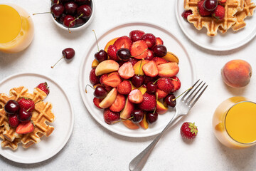 Juicy Summer fruit salad with strawberries, cherries, peach slices in plate and Belgian waffles top view. Set Morning breakfast on white background