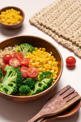 Broccoli, corn, quinoa, tomato salad in wooden bowl on light beige background. Healthy food concept