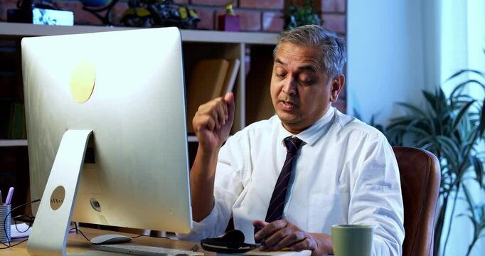 Indian call center executive in stress with overload, sitting at desk in modern office wearing headphones, Asian corporate customer service employee attending nonstop calls on computer system