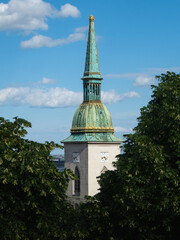 Tall green and golden spire of St. Martin's Cathedral rising above the trees in Bratislava,...