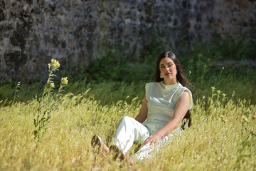 Young, pretty, brunette woman in a white dress, looking distracted, relaxed and calm, sitting in...