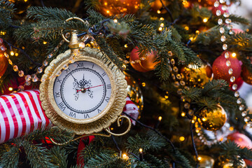 The clock hands on the dial show 12 o'clock. Golden retro clock on a Christmas tree. Beautiful...