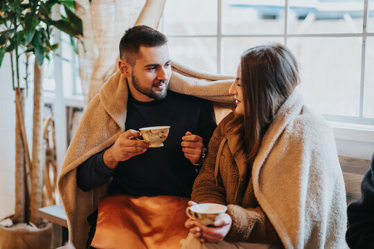 A heartfelt moment as two individuals share coffee and warmth on a chilly day, sitting indoors wrapped in a warm blanket and engaging in a meaningful conversation.
