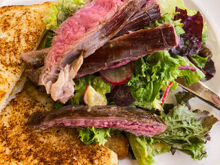 Flank steak with salad and baked toast served on white plate. Restaurant dinner