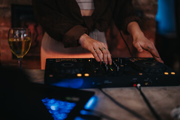 Hands with rings adjusting controls on DJ equipment during a social evening gathering.