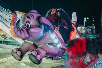 A lively scene of a nighttime funfair with colorful lights where friends ride a whimsical...
