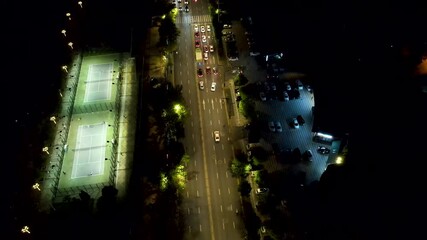 Nighttime aerial view of illuminated tennis courts and bustling city streets - Powered by Adobe