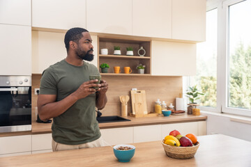Morning routine, simple living. One man standing in the kitchen, drinking coffee, eating healthy...