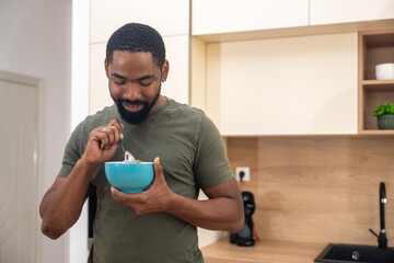 Morning routine, simple living. One man standing in the kitchen, drinking coffee, eating healthy...