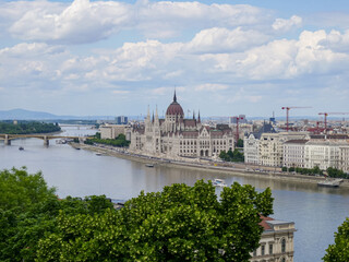 Scenic view of Hungarian Parliament Building in Budapest framed by green trees and cloudy sky from...