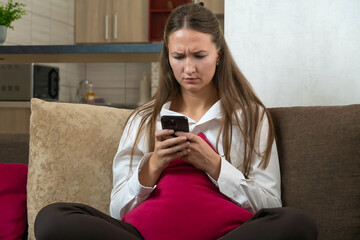 Young woman wearing white shirt using mobile phone at home, browsing internet, reading news,...