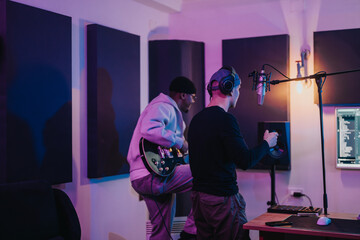 Two musicians working together in a recording studio. One is playing the guitar while the other...