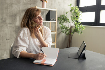 Businesswoman talking on phone and taking notes in modern office
